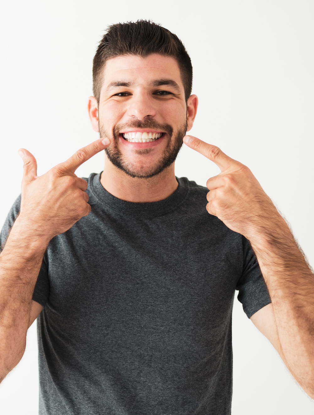 Latin man pointing to his big and bright smile. Portrait of a handsome man with white teeth is smiling and looking very happy